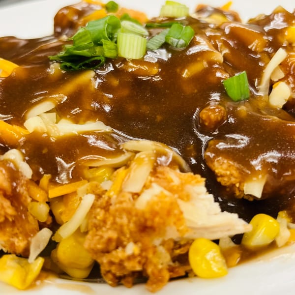 Close-up of a dish with gravy, chicken, corn, cheese, and green onions.