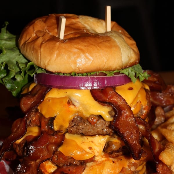 A towering Nasty's Sports Bar & Restaurant burger with multiple patties, melted cheese, bacon, onion, and lettuce.