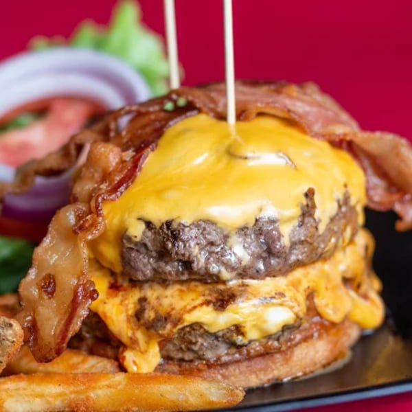 A double cheeseburger with melted cheese and crispy bacon, served with fries and a side salad.