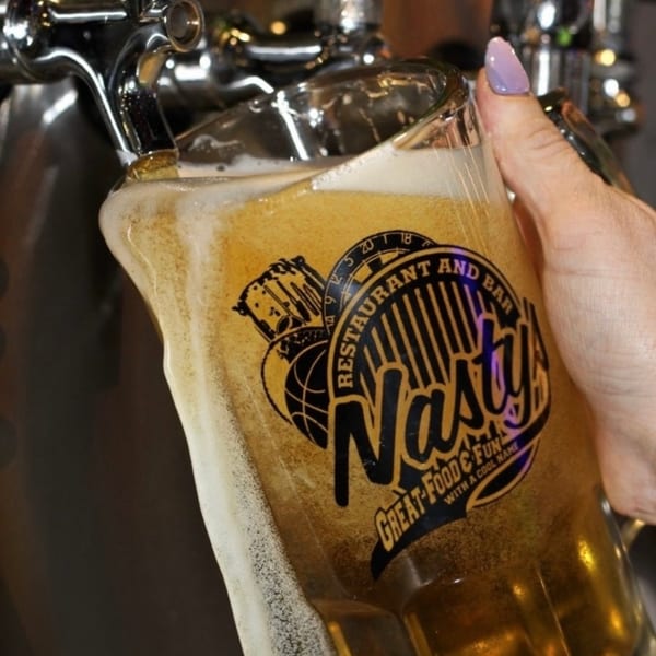 A hand holding a Nasty's branded glass being filled with beer from a tap.
