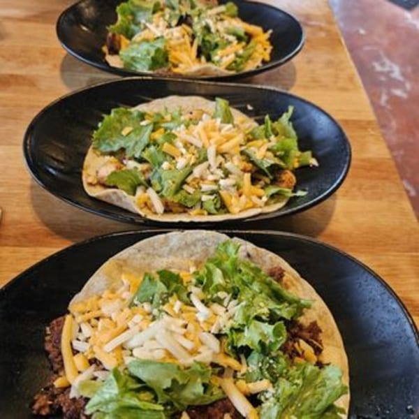 Three Nasty's Sports Bar & Restaurant tacos with meat, lettuce, and shredded cheese on black plates.