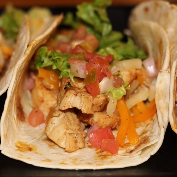 Close-up of a chicken taco with lettuce, diced tomatoes, onions, and orange peppers.