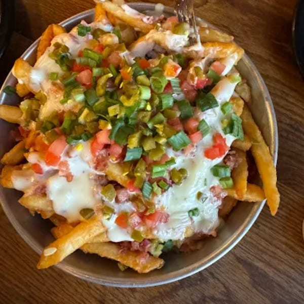 Loaded fries with melted cheese, diced tomatoes, green onions, and jalapeños in a metal bowl.